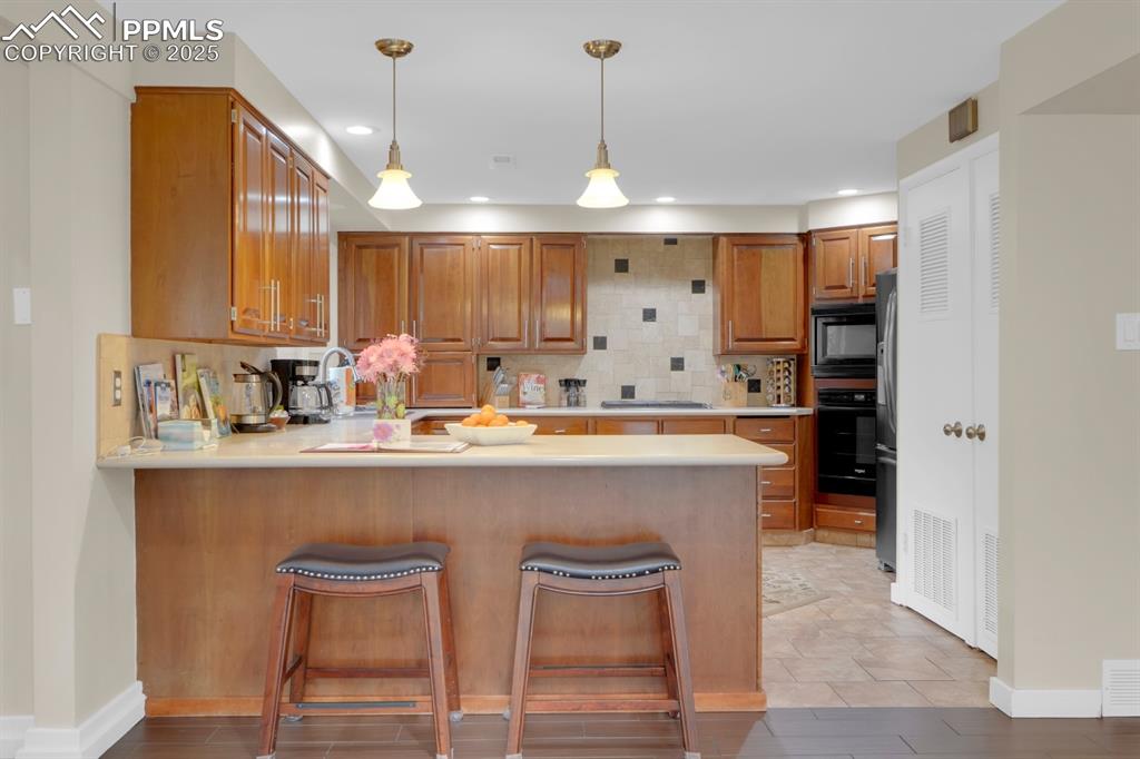 Image 19 of 43: Kitchen featuring backsplash, light countertops, a peninsula, brown cabinet