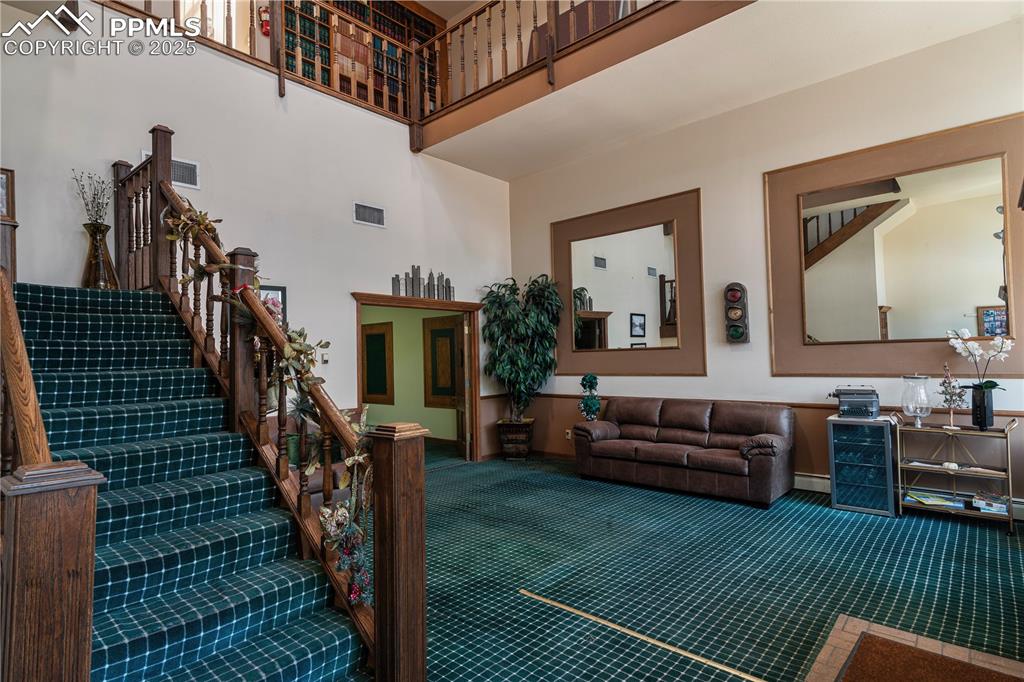 Image 13 of 31: Living area featuring a towering ceiling, carpet floors, and stairway