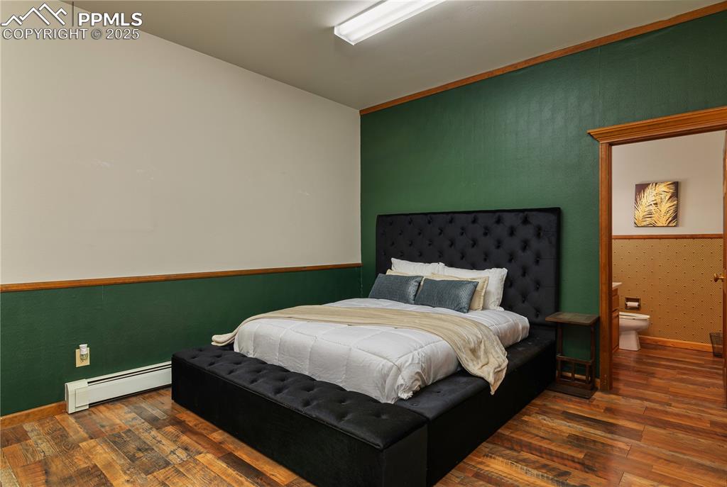 Image 19 of 31: Bedroom featuring baseboard heating, dark wood finished floors, wallpapered