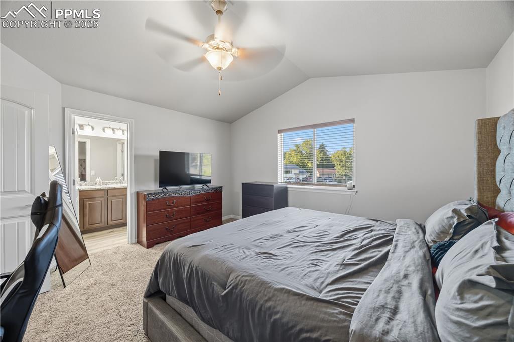 Image 18 of 33: Bedroom with vaulted ceiling, light colored carpet, a ceiling fan, and ensu