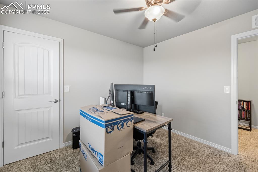 Image 25 of 33: Home office with light colored carpet and ceiling fan