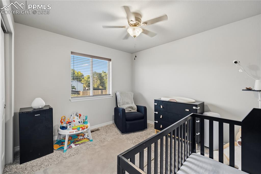 Image 28 of 33: Bedroom with a crib, carpet flooring, and a ceiling fan