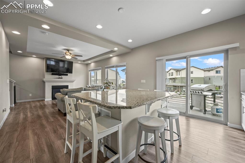 Image 10 of 44: Kitchen with wood finished floors, a ceiling fan, light stone counters, rec