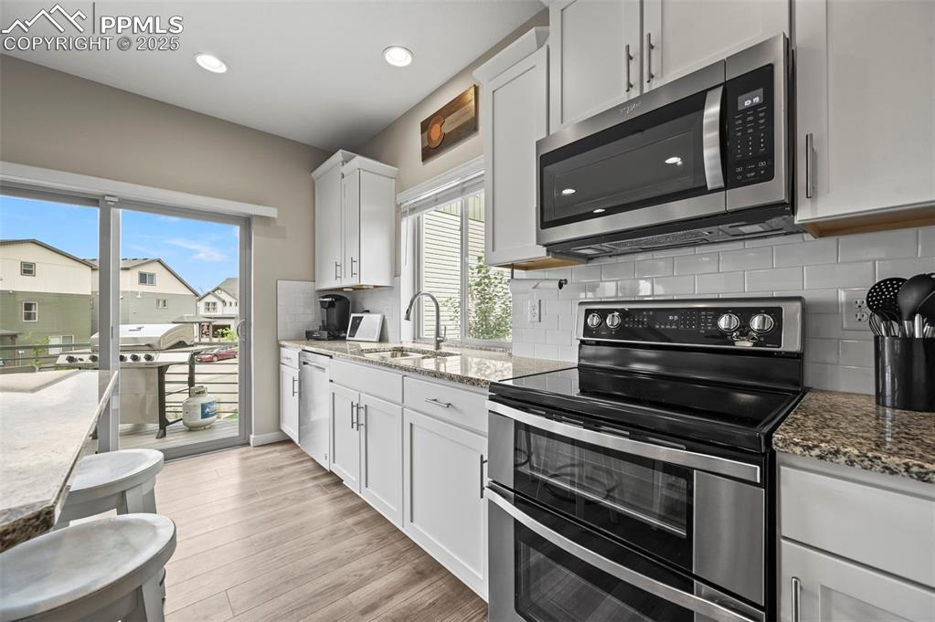 Image 11 of 44: Kitchen with stainless steel appliances, light wood-style floors, white cab