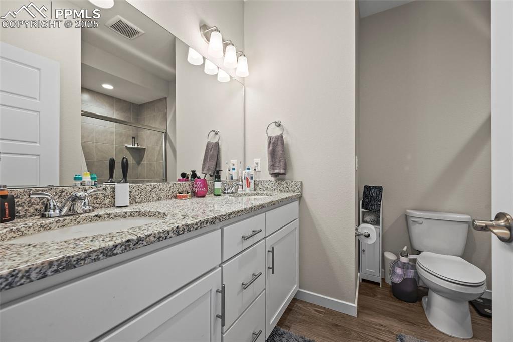 Image 16 of 44: Full bath featuring double vanity, wood finished floors, and tiled shower