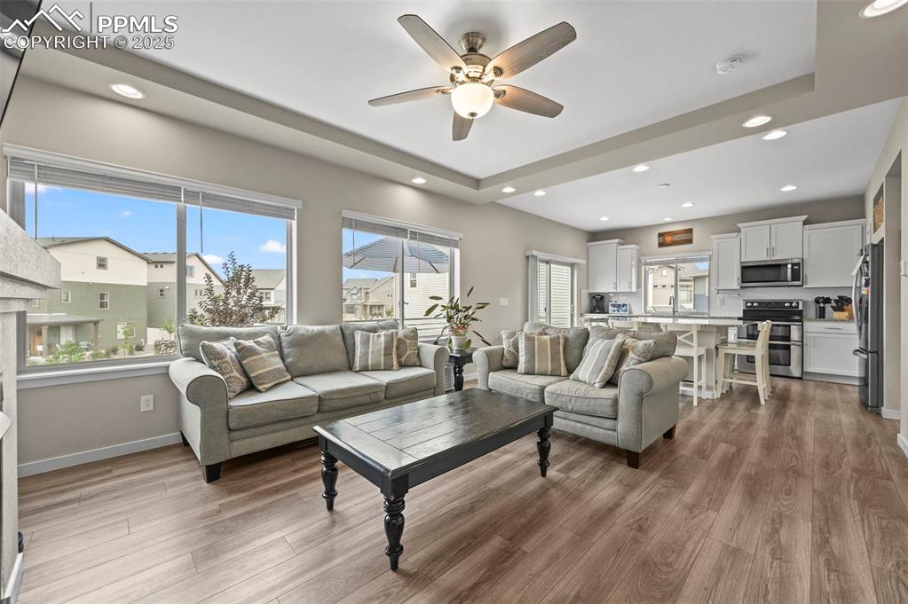 Image 4 of 44: Living area with a tray ceiling, a ceiling fan, wood finished floors, and r