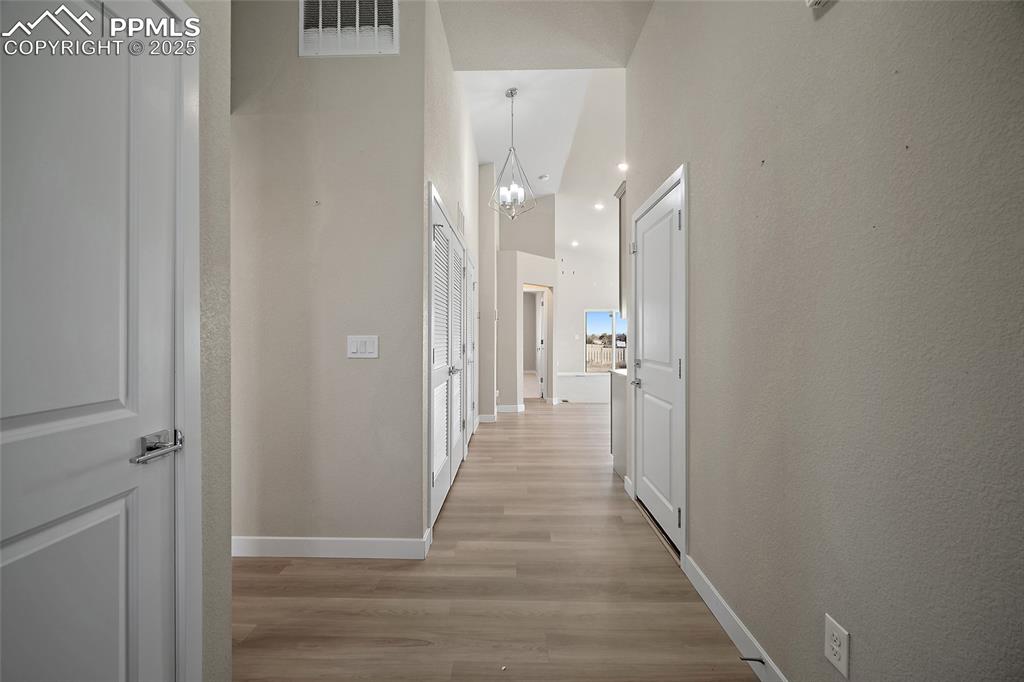 Image 19 of 30: Corridor featuring light wood-style flooring, a chandelier, a textured wall