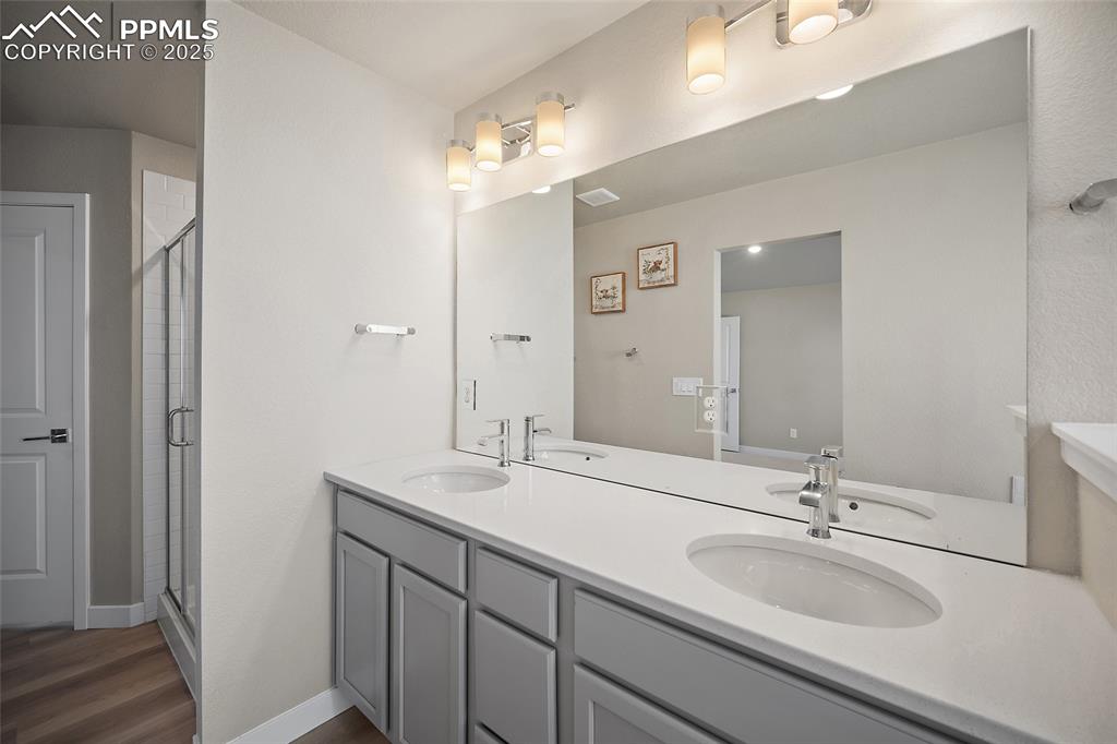 Image 28 of 30: Full bathroom with double vanity, a shower stall, and dark wood-type floori
