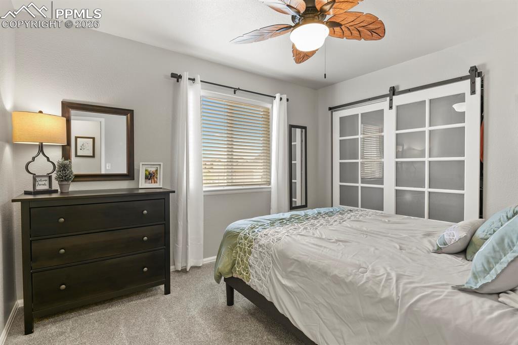 Image 32 of 40: Bedroom with light carpet, ceiling fan, and a barn door
