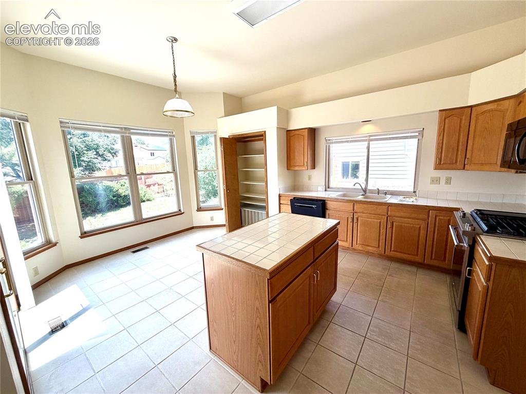Image 16 of 50: Kitchen featuring wood cabinetry, tile flooring, and a central island with