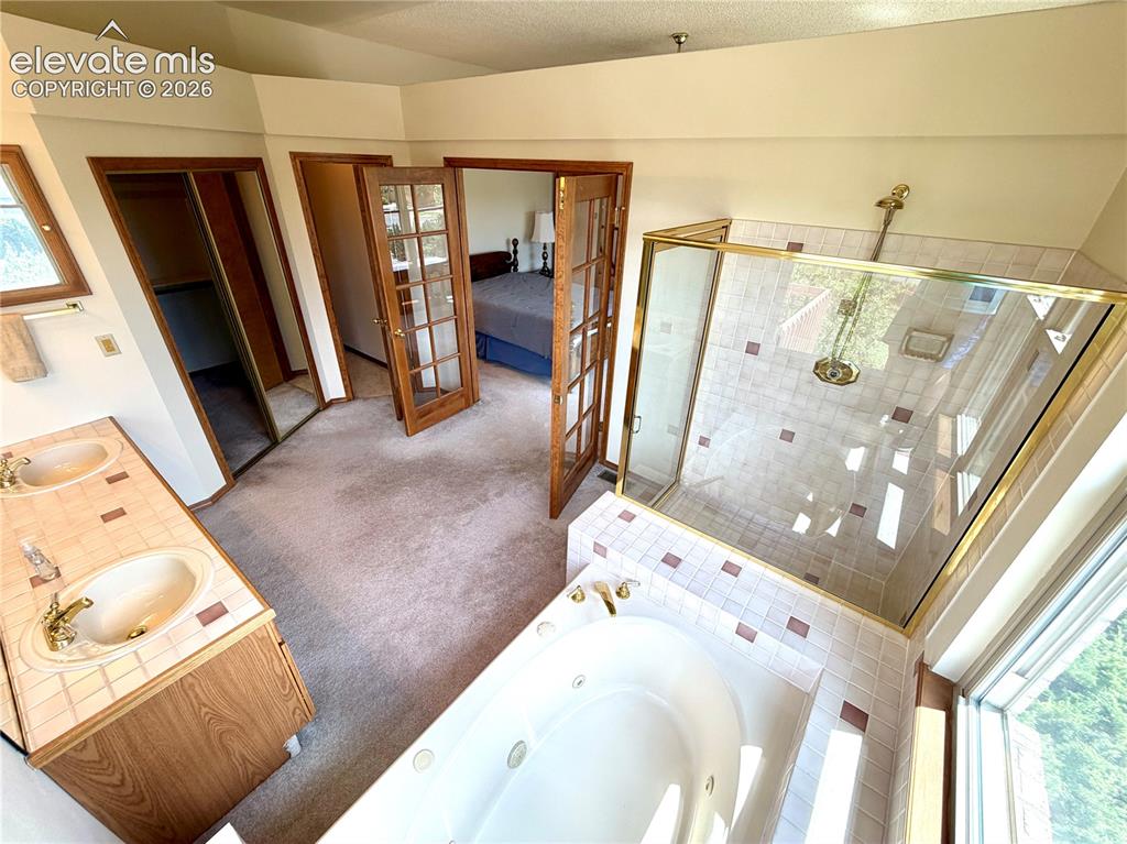Image 23 of 50: Bathroom featuring a jetted tub, glass-enclosed shower, dual vanity with ti