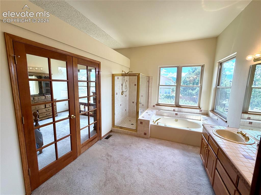 Image 25 of 50: Spacious bathroom featuring a jetted soaking tub, walk-in shower with gold-