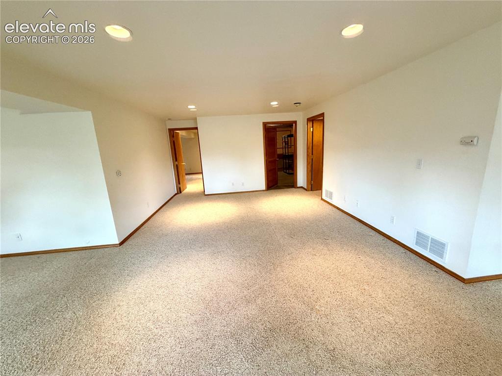 Image 47 of 50: Spacious interior room featuring light-colored carpeting, white walls, and