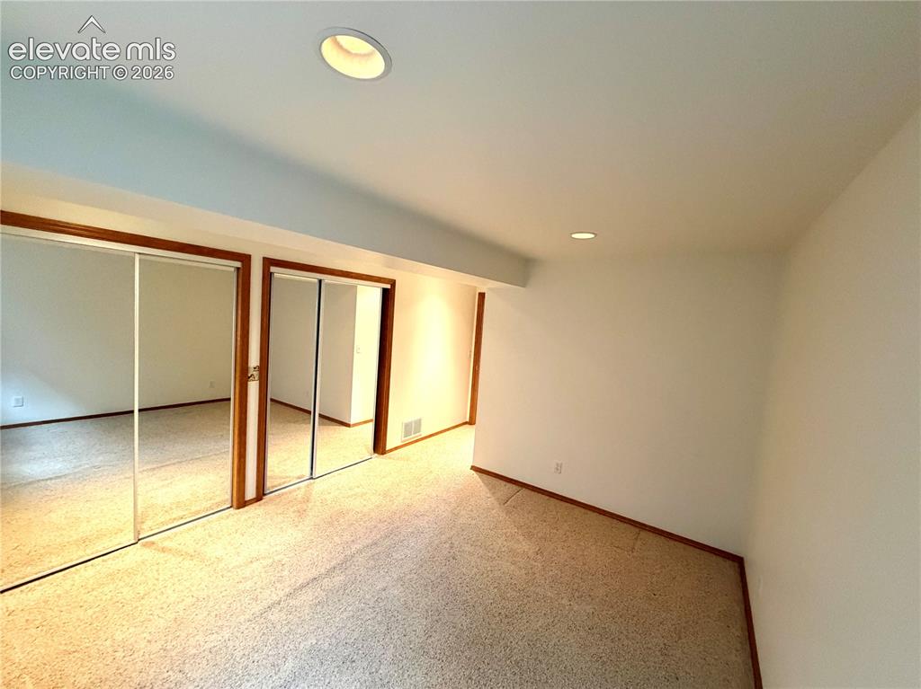 Image 49 of 50: Carpeted room with recessed lighting and two mirrored closet doors featurin