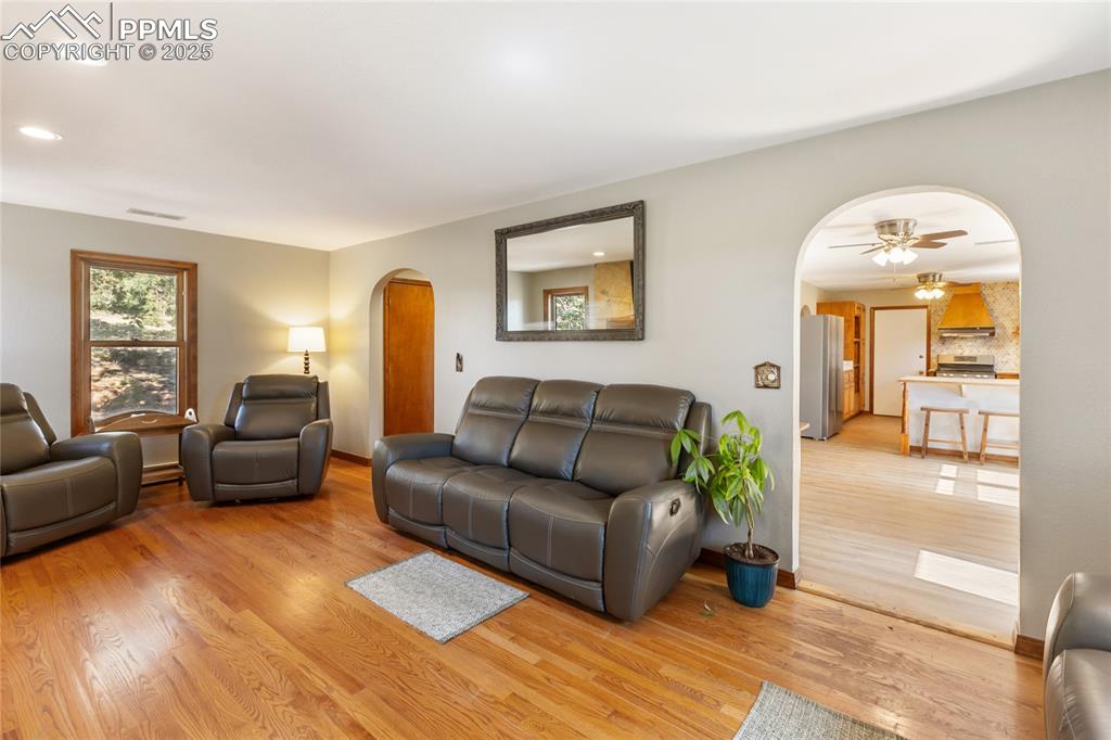 Image 14 of 50: Main level living room with hardwood flooring, arched doorways into kitchen