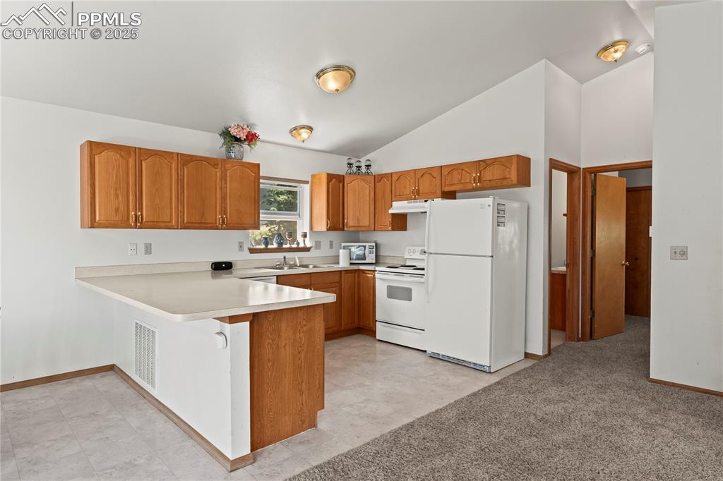 Image 11 of 36: Kitchen featuring white appliances, under cabinet range hood, a peninsula, 