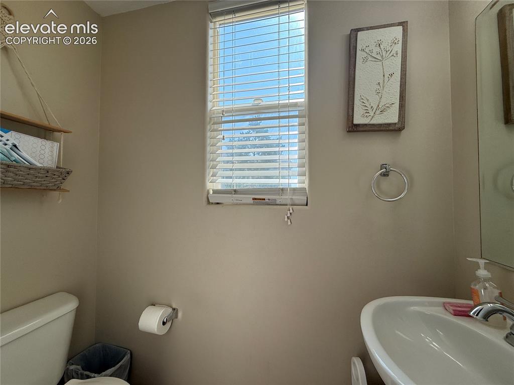 Image 11 of 27: Bright bathroom featuring a pedestal sink, toilet, and horizontal blinds al