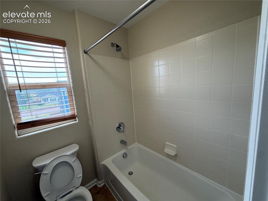 Image 16 of 28: Bathtub with white tile surround, chrome fixtures, and a window with wood b