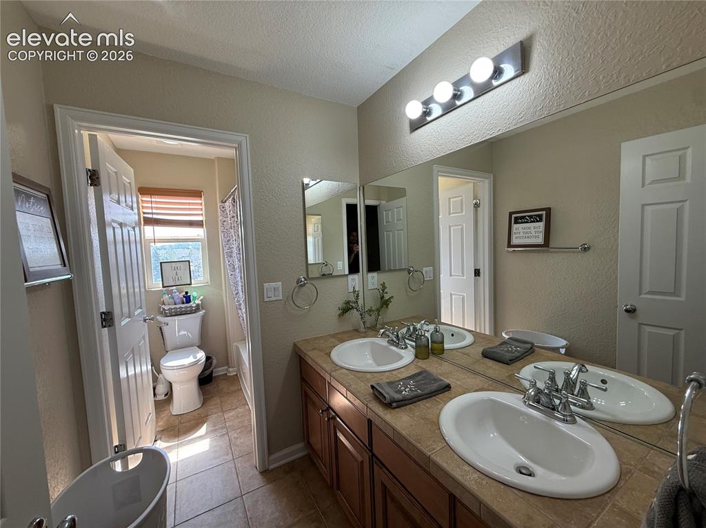 Image 19 of 27: Dual-sink vanity with wood-finish cabinetry, ceramic vessel sinks, and brus