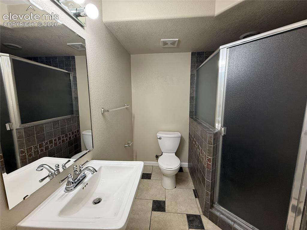 Image 23 of 28: Pedestal sink with chrome fixtures, tiled shower enclosure with frosted gla