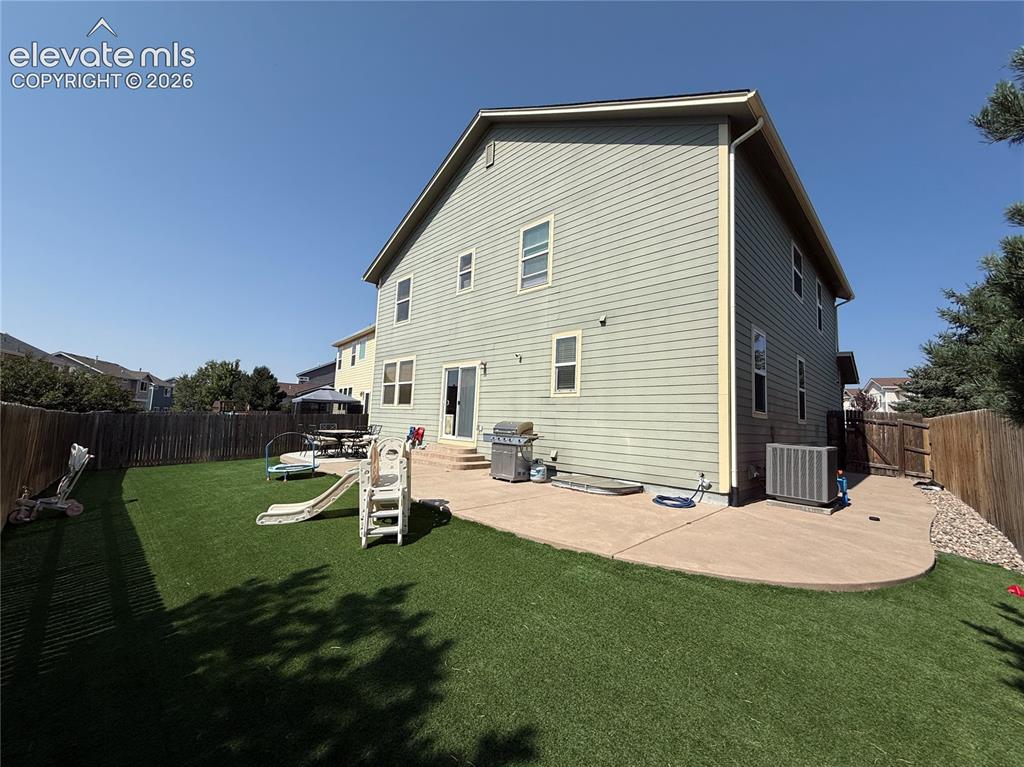 Image 25 of 27: Expansive backyard featuring artificial turf, a concrete patio, and a wood 