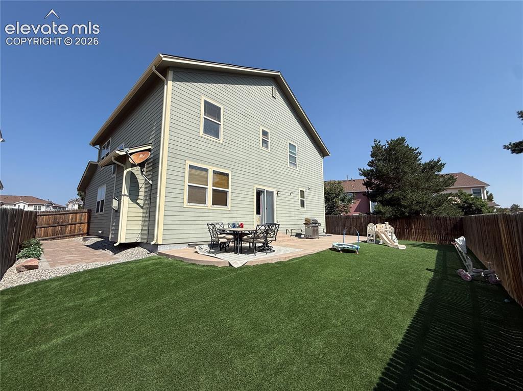 Image 27 of 27: Expansive backyard featuring a synthetic lawn, concrete patio, and brick pa