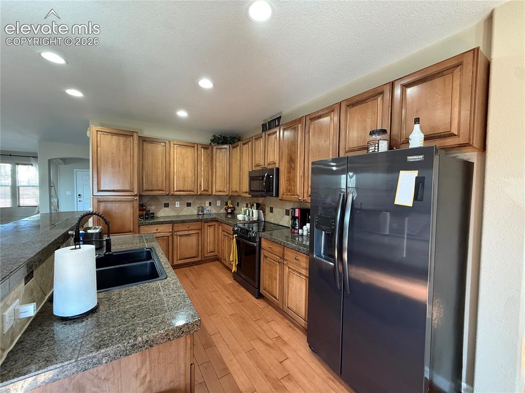 Image 7 of 27: Kitchen featuring wood-finish cabinetry, granite countertops, tile backspla