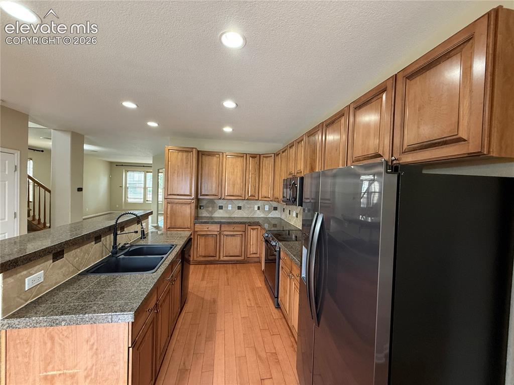 Image 9 of 28: Kitchen featuring wood-finish cabinetry, stone-look countertops, a tile bac