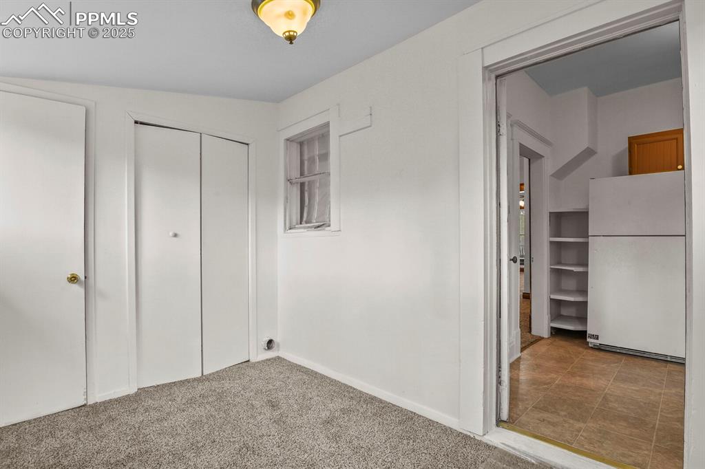 Image 28 of 30: Unfurnished bedroom with freestanding refrigerator, carpet, and a closet