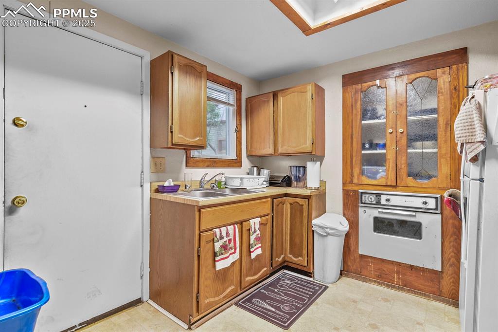 Image 7 of 30: Kitchen featuring white appliances, light countertops, brown cabinetry, and