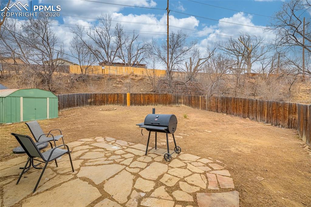 Image 29 of 29: Fenced backyard with a patio, area for grilling, and a storage shed