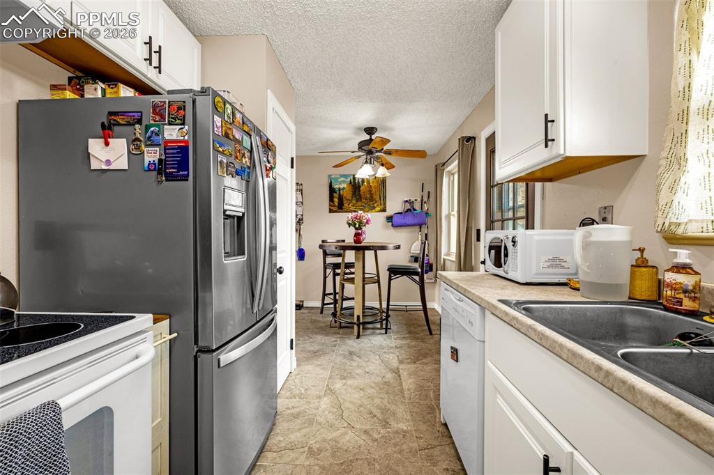 Image 9 of 29: Kitchen featuring white cabinetry, a textured ceiling, white appliances, li
