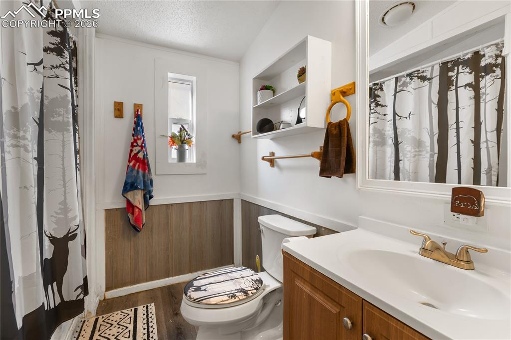 Image 19 of 27: The full bath with wainscoting, vanity, and dark wood flooring!