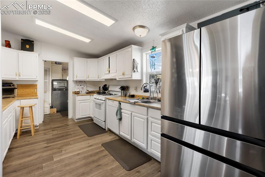 Image 3 of 27: The kitchen has white appliances, white cabinets, light countertops, and wo