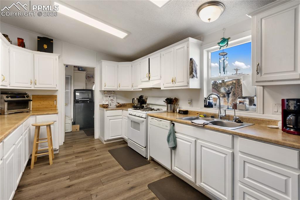 Image 4 of 27: The kitchen has white cabinets, white appliances, lofted ceiling, wood floo