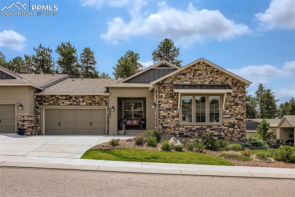 Caption: View of front of home with stone siding, driveway, and a garage