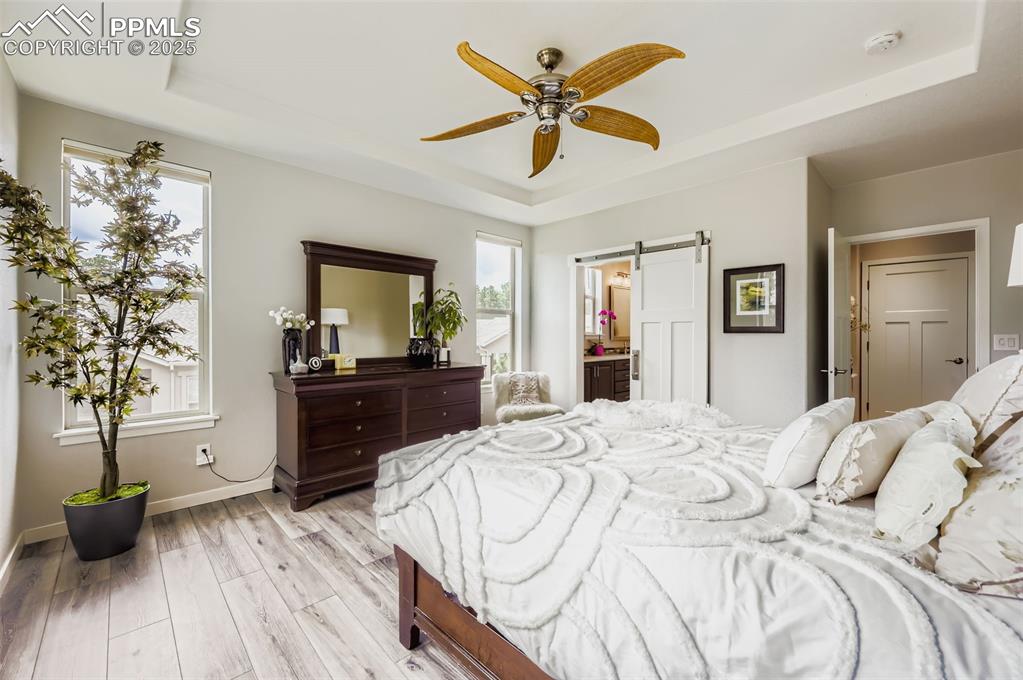 Image 22 of 50: Bedroom featuring a tray ceiling, a barn door, light wood-type flooring, a 