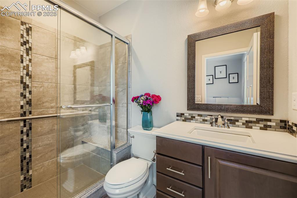 Image 28 of 50: Full bathroom with a shower stall, vanity, and backsplash