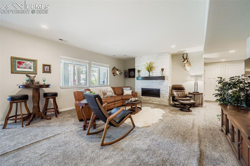 Image 30 of 50: Carpeted living area with a stone fireplace and recessed lighting