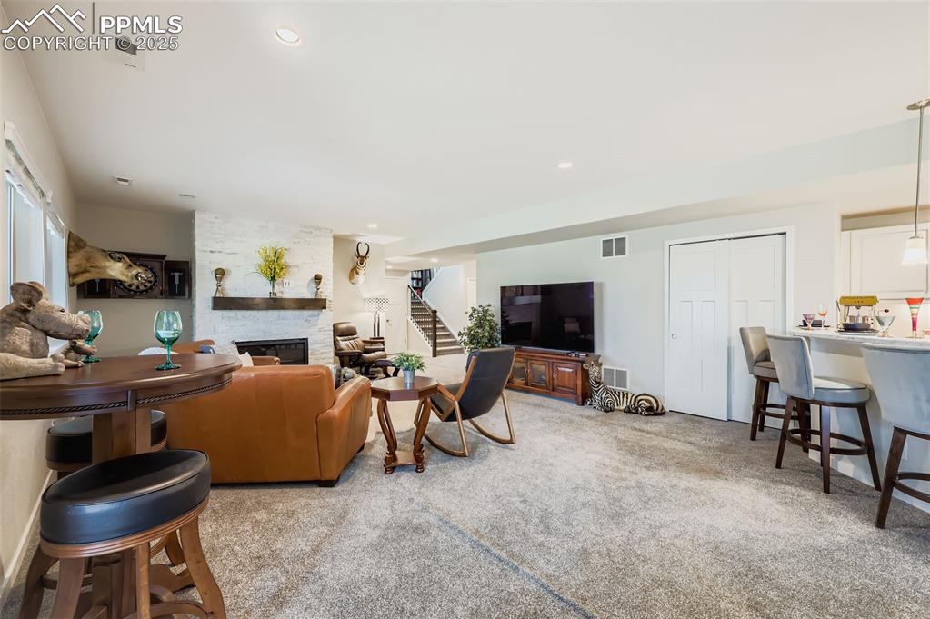 Image 31 of 50: Living area with a fireplace, stairs, light colored carpet, and recessed li
