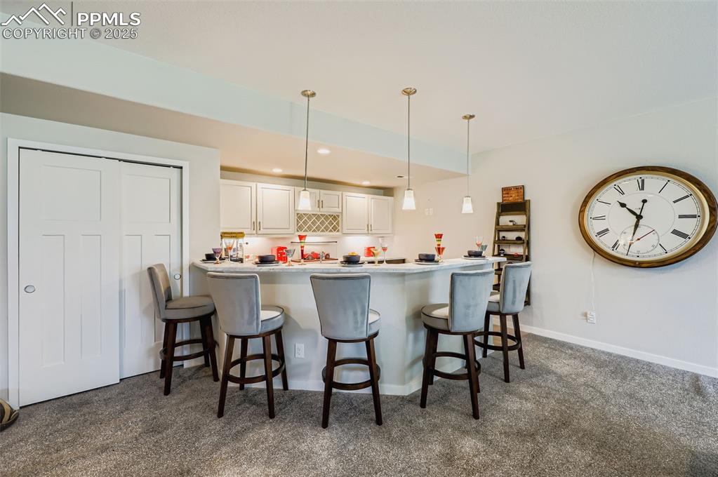 Image 43 of 50: Kitchen with white cabinetry, a peninsula, a breakfast bar area, dark carpe