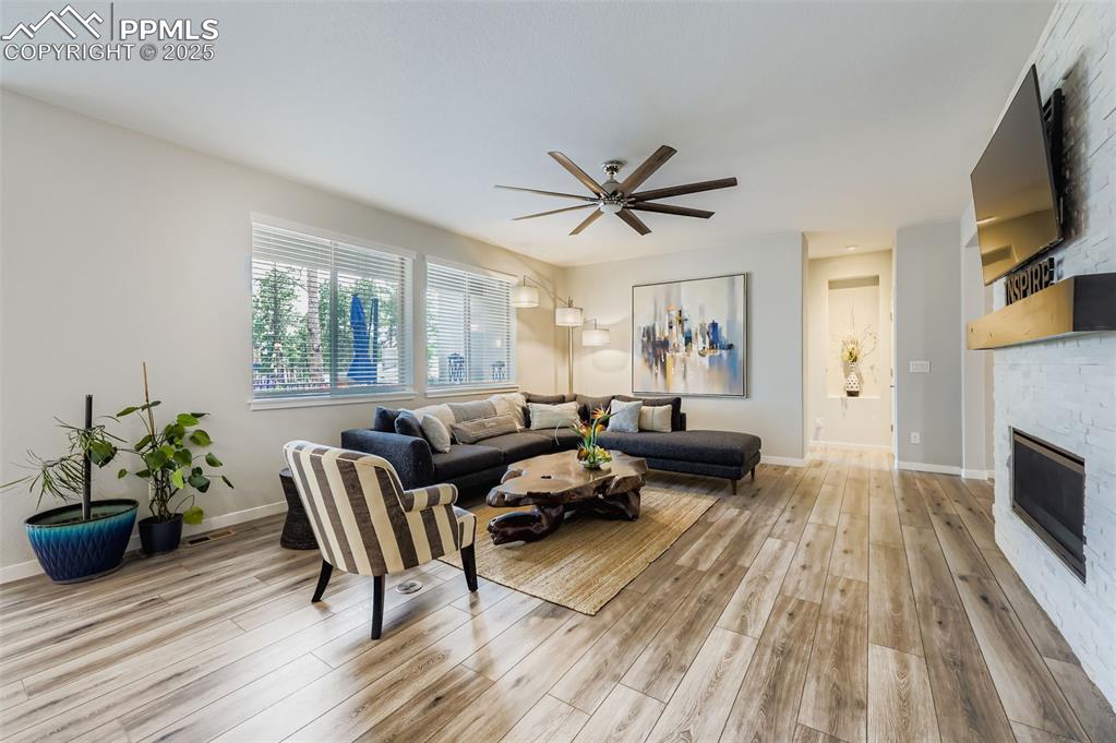 Image 9 of 50: Living area with a stone fireplace, light wood-type flooring, and a ceiling