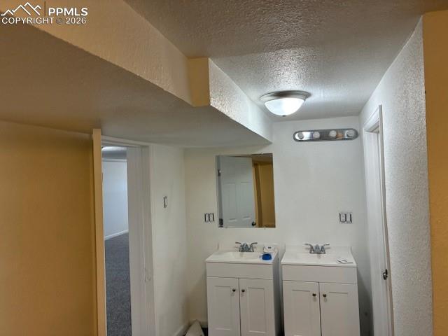 Image 19 of 24: Bathroom with two vanities, a textured ceiling, and a textured wall