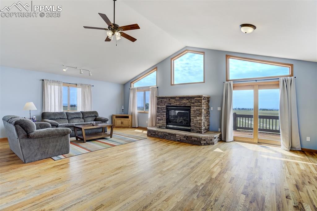 Image 16 of 50: Living area with wood finished floors, a ceiling fan, a fireplace, and high