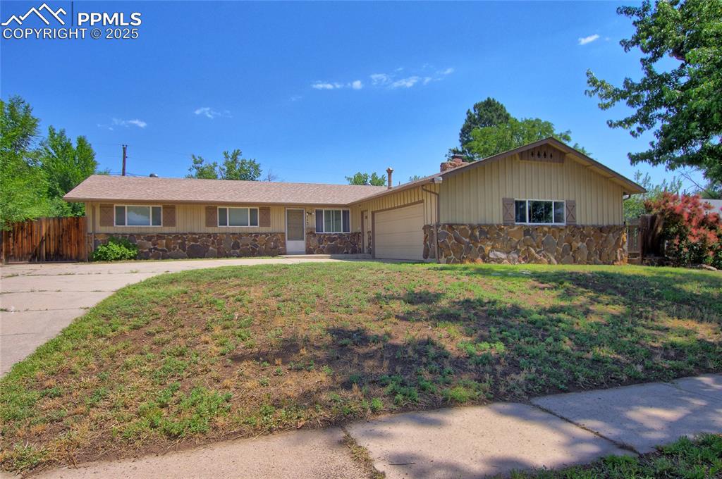 Caption: Single story home with stone siding, a garage, driveway, and a chimney