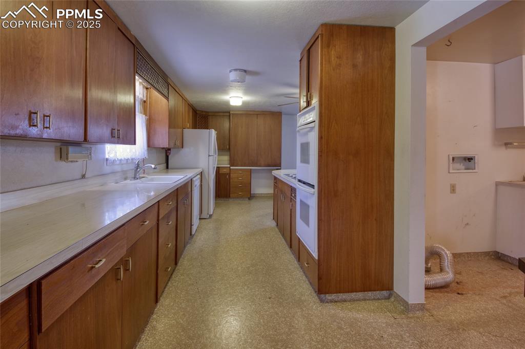 Image 10 of 37: Kitchen with brown cabinetry, light countertops, and white appliances