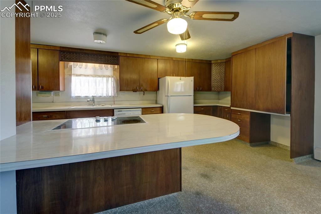 Image 11 of 37: Kitchen featuring white appliances, light countertops, brown cabinetry, and