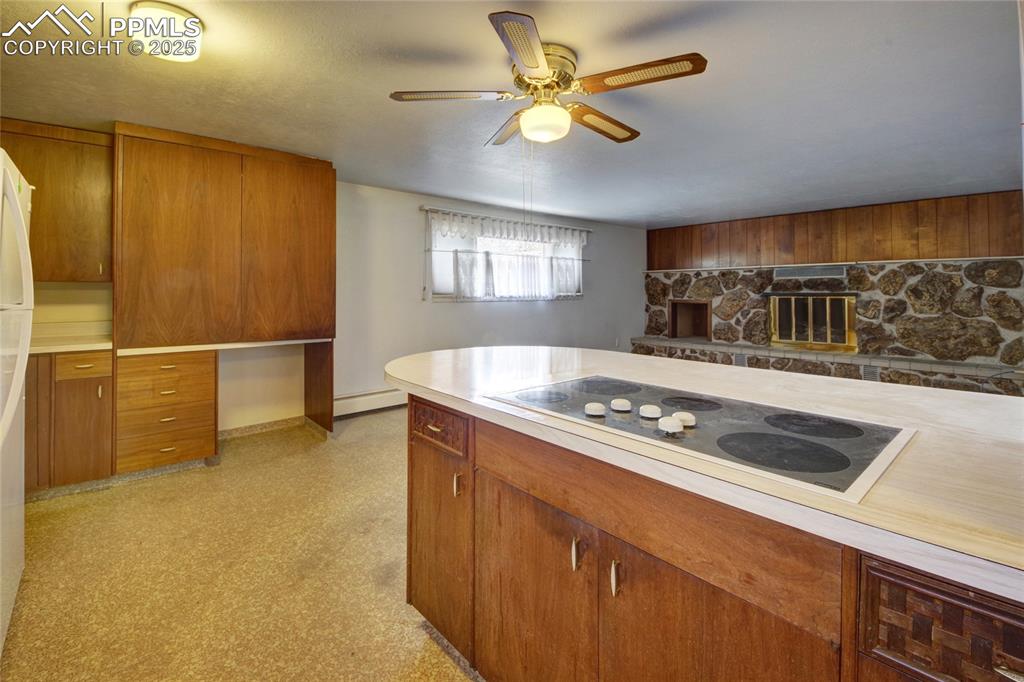 Image 12 of 37: Kitchen with ceiling fan, brown cabinets, electric stovetop, light countert
