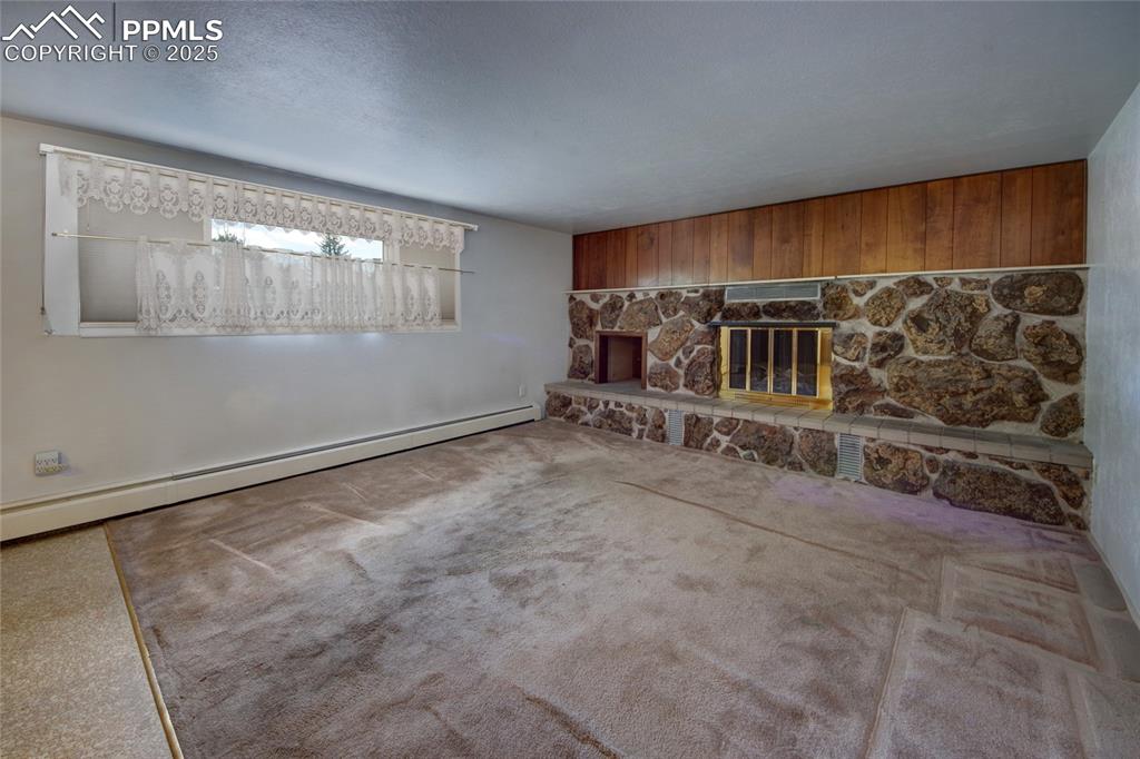 Image 15 of 37: Carpeted living area featuring baseboard heating and a stone fireplace