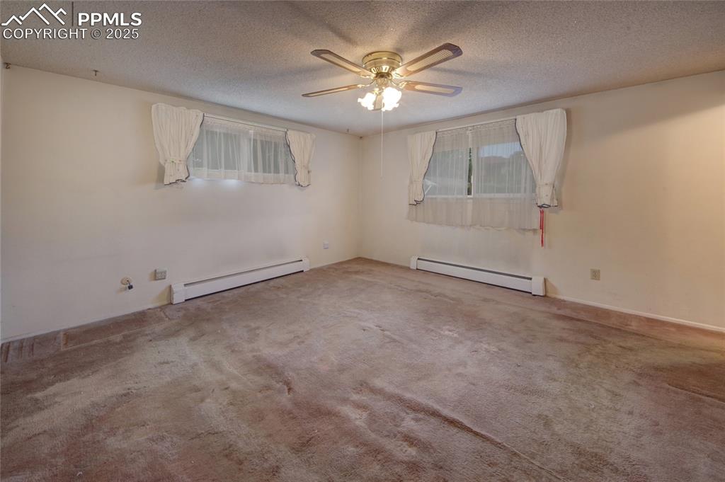 Image 18 of 37: Empty room with a baseboard heating unit, carpet flooring, ceiling fan, and